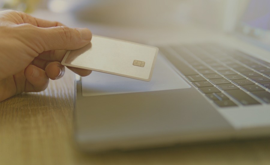 mão de uma pessoa segurando um cartão internacional na frente de um notebook