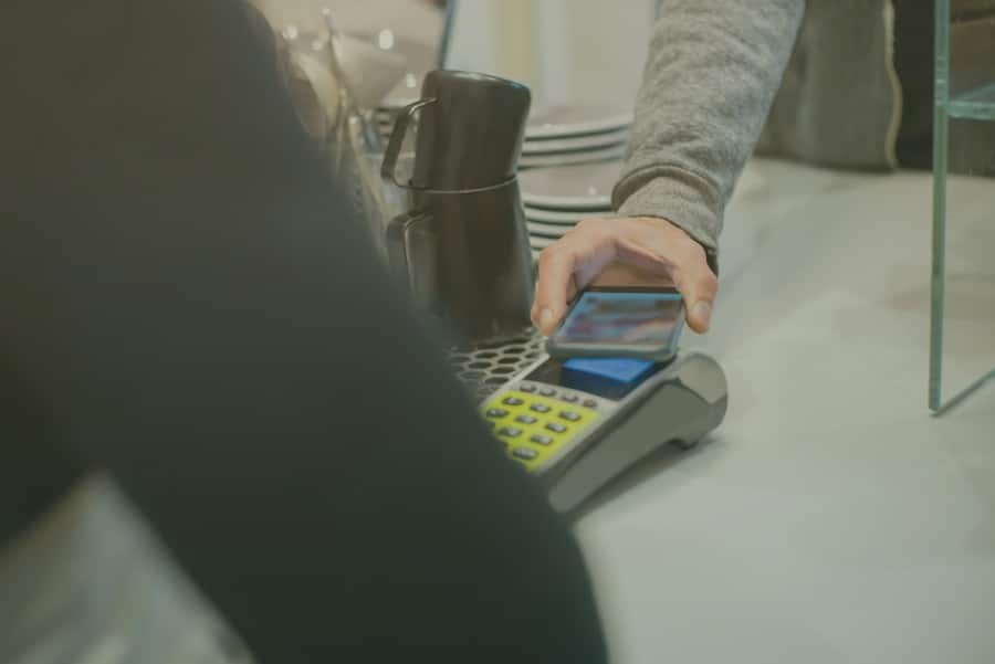 pessoa efetuando o pagamento em maquininha de loja física por meio do celular, com a carteira digital